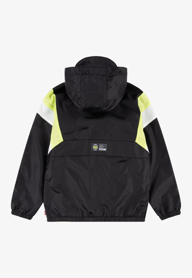 Chaqueta negra con capucha que presenta paneles de acento en amarillo neón y blanco. Está hecha de una tela suave y ligera, con puños y dobladillo elásticos.