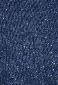 Texturiertes Gewebe in verschiedenen dunklen Blautönen, mit weißen und grünen Sprenkeln, in einem engen Strickmuster angeordnet.