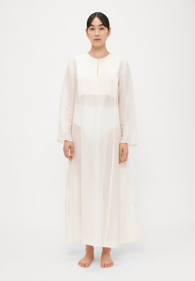 Robe légère de couleur crème avec manches longues, col rond et fentes latérales. Présente un panneau texturé au niveau du corsage.