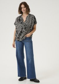 Blouse à imprimé léopard en gris clair et noir, design à col en V, manches courtes, associée à un jean bleu à jambes larges et des chaussures noires.
