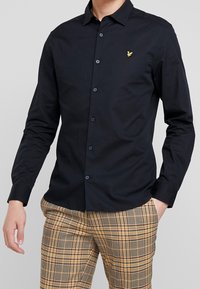 Marineblauw overhemd met lange mouwen, knopen en een mix van katoen, voorzien van een puntige kraag en een subtiel geel logo op de borst, gecombineerd met geruite broek.