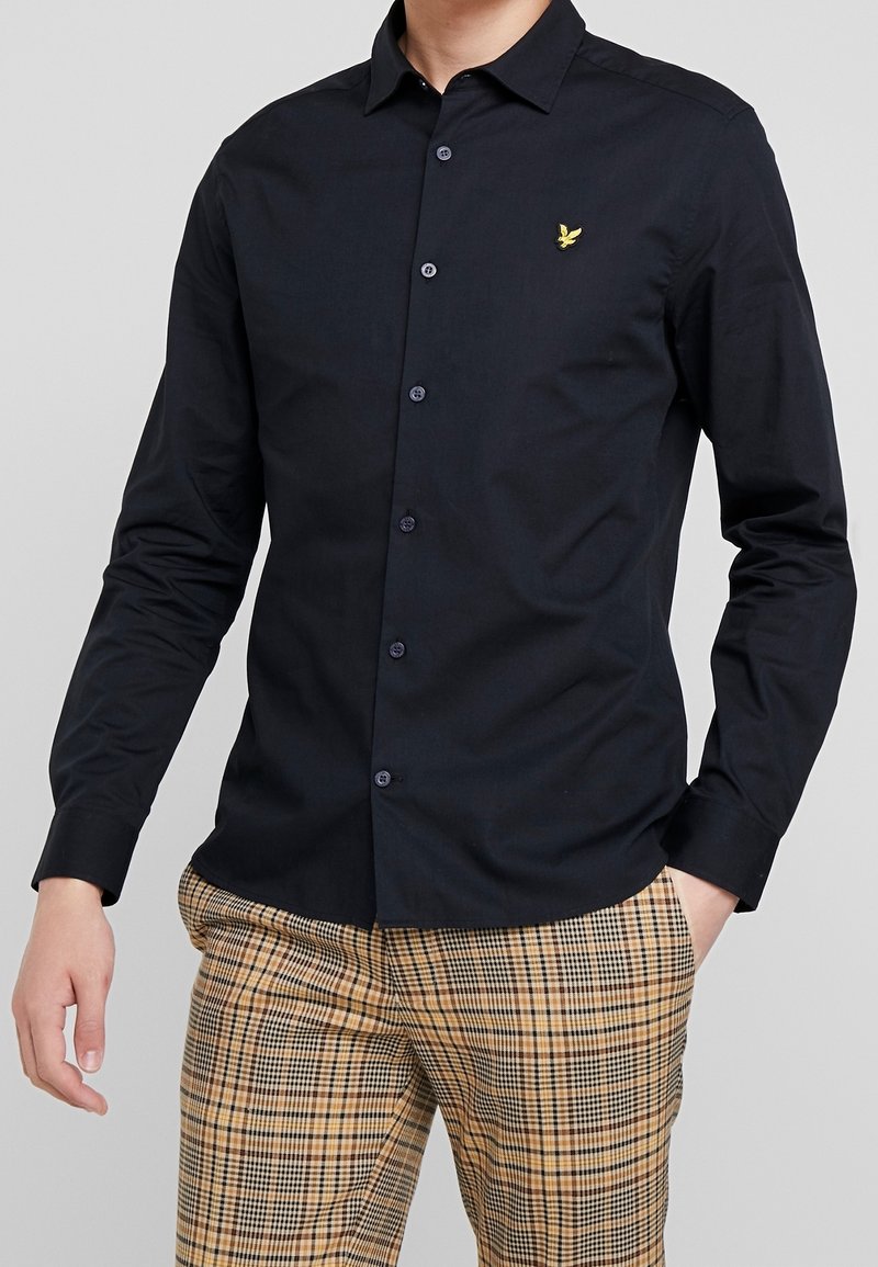 Marineblauw overhemd met lange mouwen, knopen en een mix van katoen, voorzien van een puntige kraag en een subtiel geel logo op de borst, gecombineerd met geruite broek.