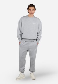 Grå sweatshirt og sweatpants sæt lavet af blødt stof, der har en løs pasform, ribbede manchetter og subtil hvid branding på brystet og låret.
