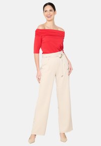 Top rosso con spalle scoperte e maniche corte, abbinato a pantaloni beige a vita alta, larghi, con una cintura in tessuto e una texture morbida.