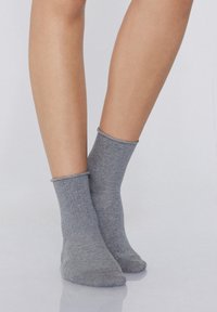 Calze in cotone grigio a manica corta con polsino a coste, superficie testurizzata e vestibilità aderente, poggiate su una superficie riflettente.