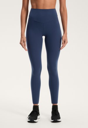 Tummansininen korkean vyötärön leggingsejä, joissa on sileä pinta, slim fit ja ei näkyviä saumoja. Yhdistetty mustiin urheilukenkään.