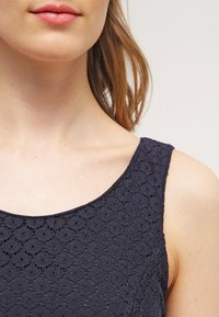 Navyblaues Spitzenoberteil mit einem gewellten Muster, das einen runden Ausschnitt und breite Träger hat. Strukturierten Stoff mit zarten floralen Details.
