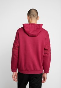 Bordeaux hoodie med känguruficka, snörning i huvan och ribbade ärmmuddar. Slät textur och avslappnad passform, med sidopaneldetaljer.