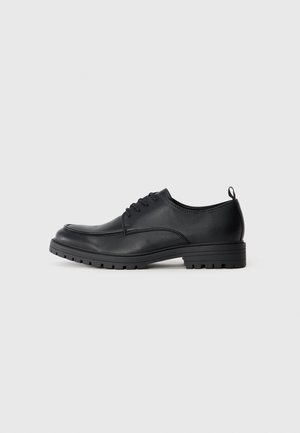 Zapato de vestir de cuero negro con textura suave, puntera redondeada, cordones delanteros y suela de goma resistente con un patrón de relieve.