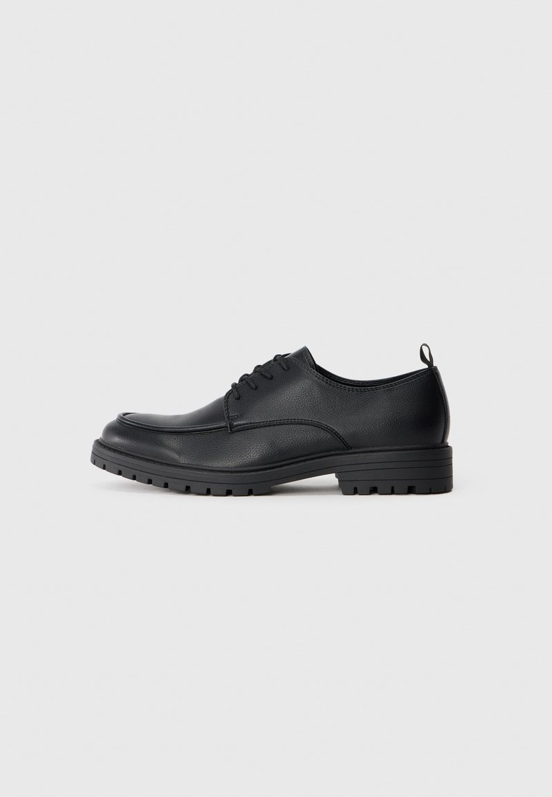 Zapato de vestir de cuero negro con textura suave, puntera redondeada, cordones delanteros y suela de goma resistente con un patrón de relieve.