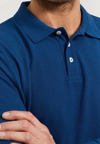 Mörkblå polo skjorta med strukturerad tyg, krage och tre vita knappar vid halsen. Tyget verkar slätt och andas.