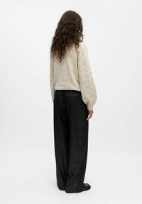 Cremefarbener Strickpullover mit strukturierten Ärmeln, kombiniert mit schwarzen, weit geschnittenen Hosen. Das Outfit zeichnet sich durch eine lockere Passform und ein minimalistisches Design aus.