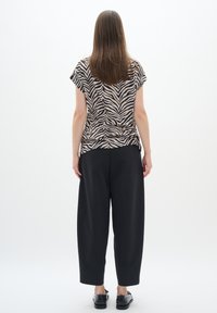 Top a maniche corte beige con strisce zebra nere; indossato con pantaloni neri a vita alta; tessuto liscio; vestibilità comoda.