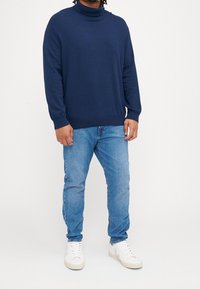 Mörkblå polotröja i mjukt material, med långa ärmar och ribbade muddarmar. Matchad med ljusblåjeans och vita sneakers.