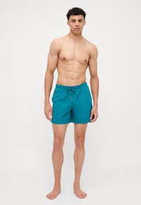 Shorts de bain teal en tissu léger, dotés d'une taille élastique avec cordon de serrage et de poches latérales. Design simple et épuré.