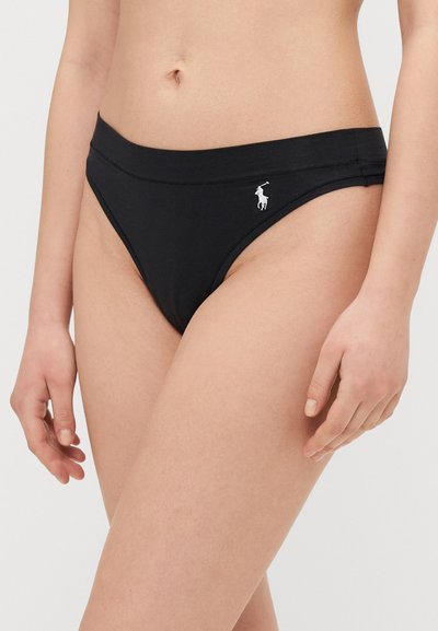Melna kokvilnas bikini apakša ar gludu tekstūru, plašu jostu un baltu logotipa akcentu sānos. Minimālistisks dizains.