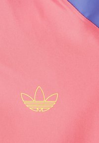 Pink fabric with a smooth texture, featuring a yellow Adidas logo in a flower-like design at the bottom. Blue accents in the top corner.