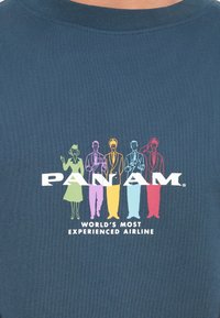 Navyblauw T-shirt met vijf kleurrijke figuren in verschillende outfits. Er staat "PAN AM" en "DE MEEST ERVAREN LUCHTVAARTMAATSCHAPPIJ TER WERELD" onder.