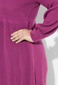 Pletené magentové šaty s ribovanou texturou, dlouhými rukávy a přiléhavým pasem, s bočními panely pro tvar a pohyb.