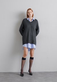 Pulover supradimensionat de culoare gri închis cu decolteu în V, purtat peste o rochie cămașă de culoare albastră deschisă. Sosete negre până la genunchi și pantofi cu vârf ascuțit completează ținuta.