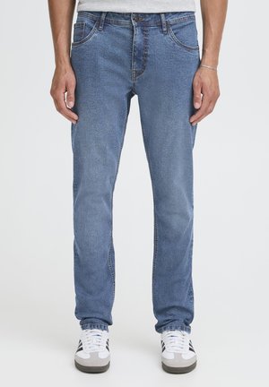 Jeans de mezclilla azul con ajuste slim, cinco bolsillos, efecto de desgaste ligero y costuras contrastantes, combinados con zapatillas blancas.