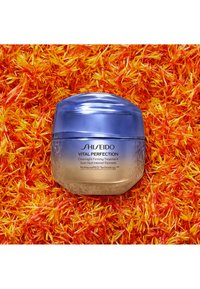 Shiseido Vital Perfection Overnight Firming Treatment i en rundad glasburk med en gradient från blå till frostig bärnsten, med präglad märkning.