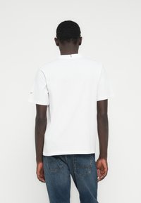 Λευκό κοντομάνικο βαμβακερό μπλουζάκι με λαιμόκοψη και μια διακριτική ραφή στο πίσω μέρος, συνδυασμένο με μπλε τζιν παντελόνι.