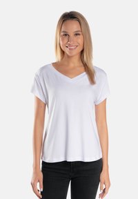 Biała koszulka polo z krótkim rękawem, wykonana z miękkiego materiału, w luźnym kroju, z podwiniętymi rękawami i gładką fakturą, połączona z czarnymi dżinsami.