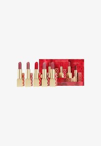 Sette rossetti Estée Lauder in astucci dorati, con tonalità che variano dal nude al rosso, allineati di fronte a una confezione della serie limitata rossa.