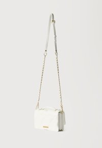 Μικρό λευκό τσάντα ώμου με καπιτονέ σχέδιο, χρυσή αλυσίδα ιμάντα και προσαρμόσιμο λευκό δερμάτινο τμήμα, κρεμασμένη σε απλό ανοιχτό φόντο.