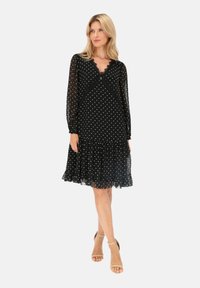 Czarna sukienka w kropki z długimi rękawami, dekoltem w kształcie V i falbaną na dole. Wykonana z przezroczystego materiału, z luźnym fasonem i delikatnymi koronkowymi akcentami.