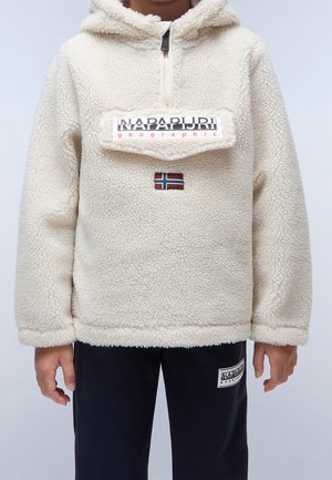 Barn iført en cremefarvet fleece-pullover med lynlås og Napapijri-logo på lommen, kombineret med sorte bukser med en matchende logopatch.
