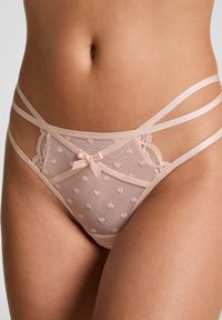 Doorzichtig roze lingerie met hartpatronen, kantafwerking en satijnen bandjes. Een klein strikje in het midden voegt een delicate accentdetail toe.