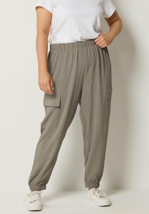 Person trägt lose graue Cargo-Hose mit elastischem Bund und Bündchen, kombiniert mit weißen Sneakers und einem weißen kurzärmligen Oberteil.