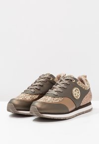 Braune Sportschuhe mit einer Kombination aus glatten und strukturierten Materialien, goldenen Akzenten und einem gemusterten Textiloberteil.