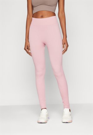 Leggings de canalé rosa claro con una cinturilla alta, combinados con zapatillas deportivas blancas con acentos morados.
