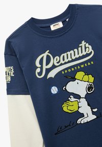 Granatowa bawełniana koszulka z dużą grafiką przedstawiającą Snoopy'ego w żółtej czapce i trzymającego rękawicę, z napisem "Peanuts Sportswear".