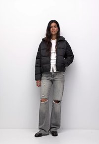 Črna puhovka s kapuco, vodoravni quilted vzorec, nosi se preko bele majice. V kombinaciji s svetlo sivo denim hlačami z raztrganinami na kolenih.