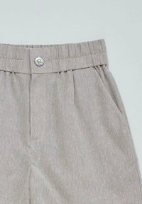 Pantalones de tejido acanalado color beige claro con cinturilla elástica, un botón decorativo y bolsillos laterales, mostrados sobre un fondo claro y liso.