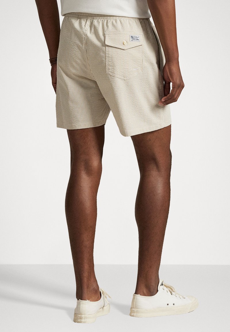Beige gestreifte Shorts aus leichtem Stoff mit elastischem Bund, einer Gesäßtasche und weißen Sneakers.