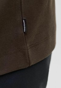 Hnědá bavlněná tričko s malou černou cedulkou "JACK & JONES" na lemu. Hladká textura s běžným střihem a prošitými detaily.