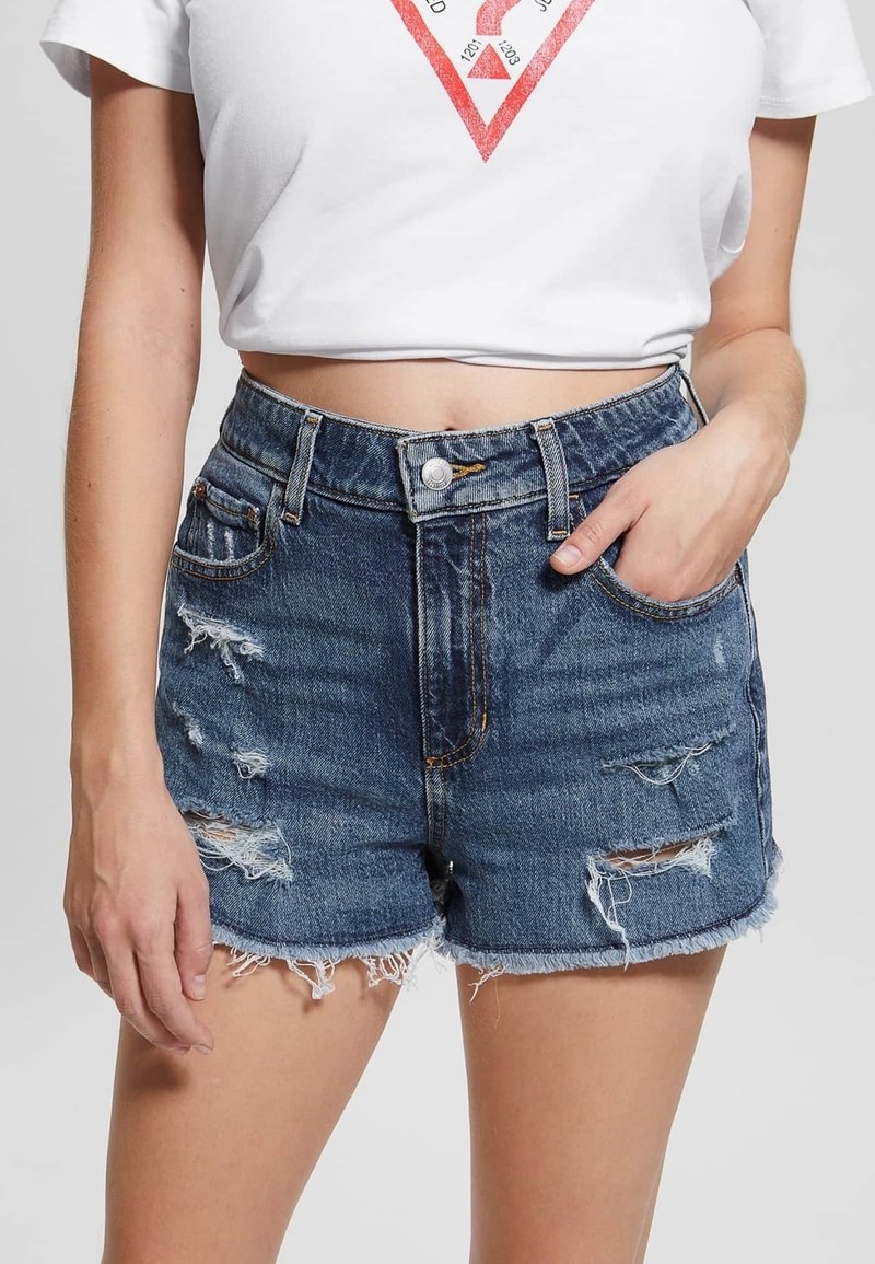 Denimshorts i mørkeblå med slidte detaljer, frynser på kanterne og femlomme-design. Knapp og lynlås foran.