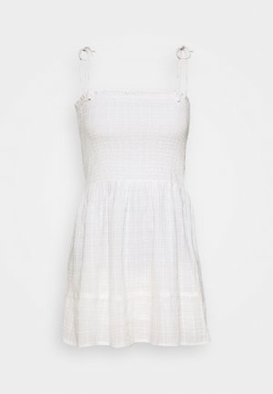 Weißes, ärmelloses Kleid mit gerafftem Oberteil und fließendem Rock. Hergestellt aus leichtem Stoff, mit verstellbaren Schulterbändern und einem gestuften Saum.