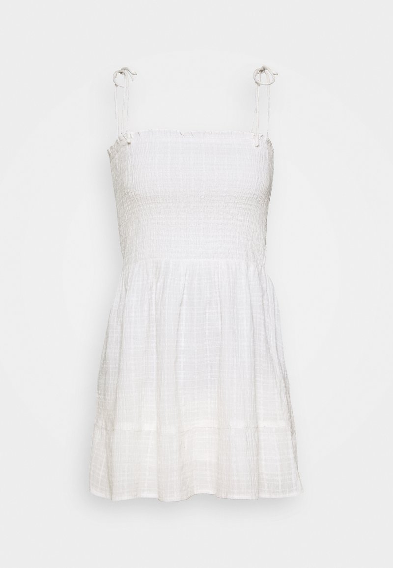 Bílé šaty bez rukávů se smocked korzetem a splývavou sukní. Vyrobené z lehkého materiálu, s nastavitelnými ramínky a vrstvovaným lemem.