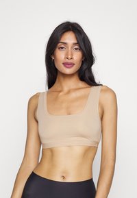 Beige sömlös bralette med fyrkantig halsringning, breda remmar och strukturerad tyg. Har en åtsittande passform och minimalistisk design.