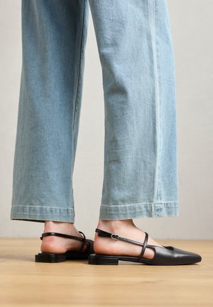 Sorte læder slingback-sko med spidse tæer, flad hæl og ankelrem; båret med lyseblå viddebenede jeans.