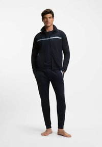 Marineblauw jack met rits en hoge kraag, met witte streepdetails, gecombineerd met bijpassende taps toelopende broek, gemaakt van zacht en rekbaar materiaal.