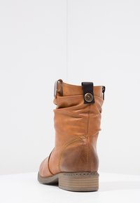Bottine en cuir marron avec un design froncé, surface texturée, accents cousus et un détail en métal circulaire sur le talon.
