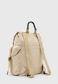 Beige rugzak met een quilted textuur, verstelbare tan schouderbanden met rode stiksels, en een gevlochten zwarte handgreep aan de bovenkant. Inclusief zijvak.