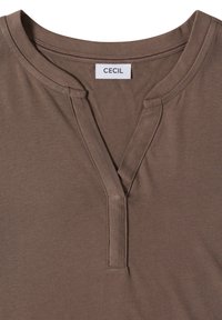 Chemise en coton marron avec un col rond fendu et une étiquette de marque visible "CECIL" cousue à l'intérieur du col.